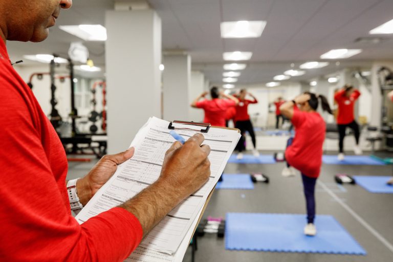 a person writing on a clipboard while people exercise in the background